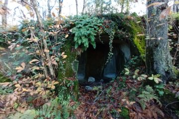masso di tufo verde, ricoperto da muschio e vegetazione, scavato dall'uomo per farne un rifugio.